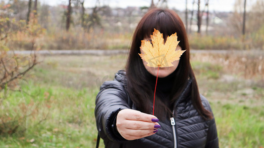 女孩在她面前拿着一片黄色的枫叶。