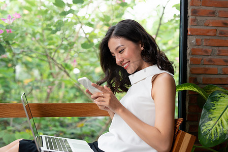 在咖啡店内休息时，微笑的年轻女性在手机上阅读短信