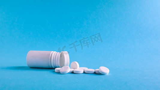白色药丸和白色塑料小瓶，深蓝色背景上有复制空间，健康和医学概念。