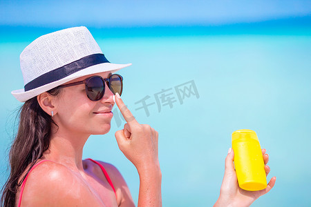白沙滩上，年轻快乐的女人在鼻子上涂防晒霜