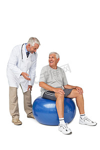 老人摄影照片_男性治疗师看着老人坐在健身球上
