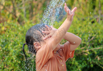 浴缸背景摄影照片_可爱的亚洲小女孩在夏日花园里玩喷水软管很有趣。