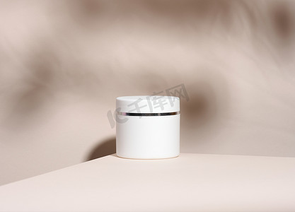 桌子上的罐子摄影照片_米色桌子上的化妆品白色罐子。