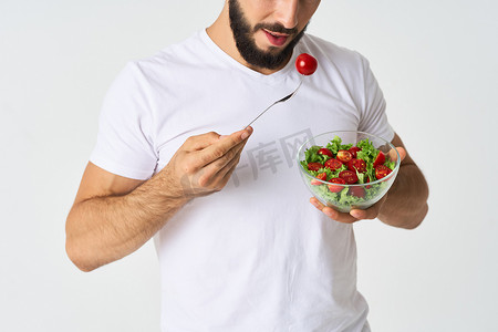 一个穿着白色T恤的男人，盘子里放着沙拉和零食健康食品