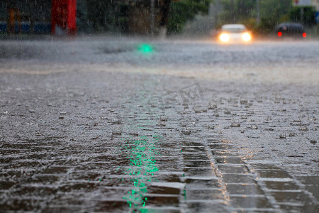 城市大雨摄影照片_十字路口的大雨和红绿灯的绿灯在城市街道上反射成大滴和水流。