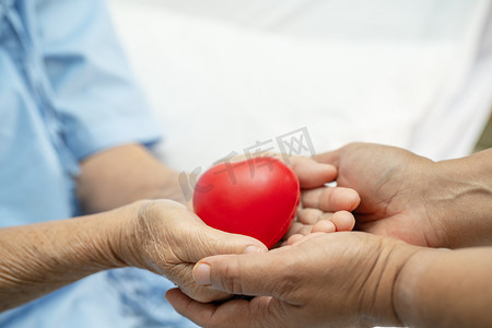 亚洲老年或老年老妇人病人在护理医院病房的床上手握红心，健康强健的医疗理念