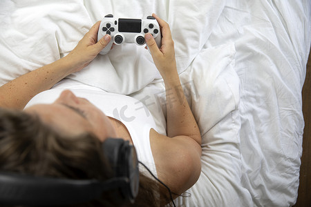 女人躺在床上用游戏控制器玩电子游戏，白床单顶视图有复制空间，游戏，控制台概念