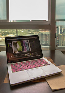 在窗边的工作区度过愉快的一天，在早晨的阳光下有一台带有城市背景的笔记本电脑。