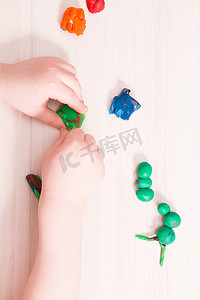 一个小孩在木桌上用绿色橡皮泥雕刻毛毛虫，手部精细运动技能的发展，在家里和孩子玩耍，前景中用橡皮泥雕刻毛毛虫