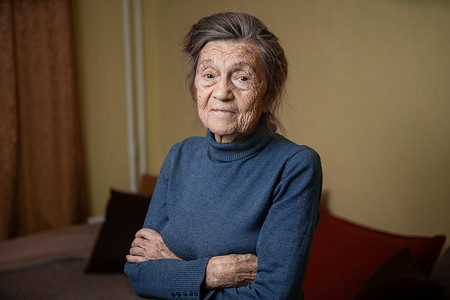 灰白摄影照片_九十岁的白种人老奶奶专注地看着，微笑着，感觉很高兴，大肖像，脸上有深深的皱纹，灰白的头发。