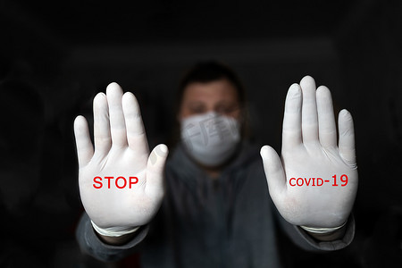 一名戴着医用口罩和手套的男子用两只手展示“停止”，深色背景上写着红色文字“停止 COVID 19”。