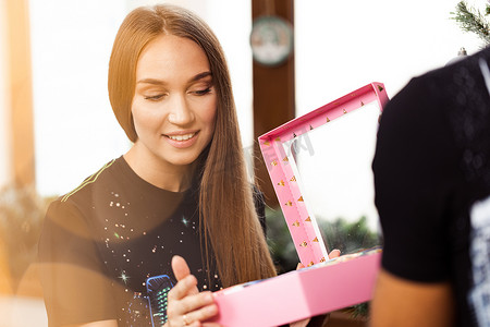 惊讶的年轻女子打开了一个粉红色的盒子，里面装着礼物。