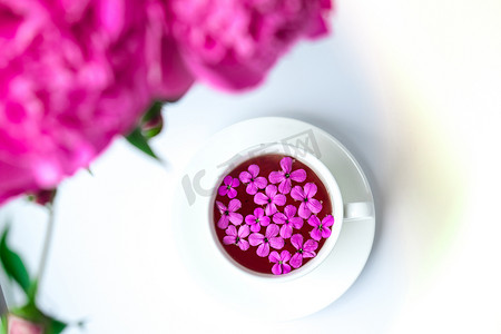 明亮的桌子上有粉红色牡丹花和一杯茶的创意布局。