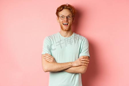 戴着眼镜的快乐欧洲男人的肖像，看着镜头惊奇，看到有趣的促销活动，站在粉红色背景中被逗乐了