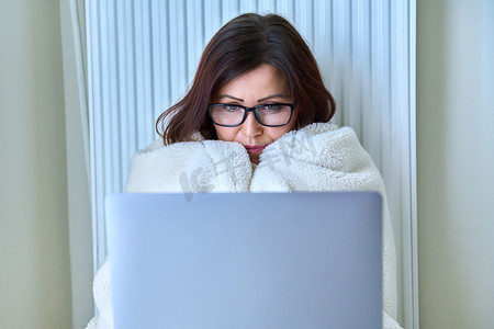 带笔记本电脑在家工作、用毯子和暖气片取暖的女性