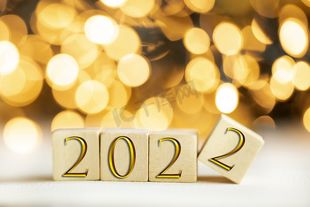 金色2022摄影照片_2022 年写在木制立方体上，金色豪华字母带有闪亮的散景背景，新年庆祝概念闪闪发光