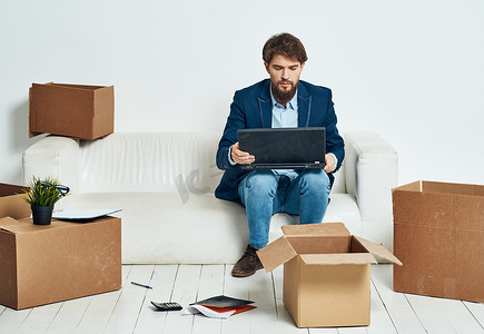 一个男人坐在笔记本电脑前的沙发上，工作箱里装着东西，正在打开新办公室的包装