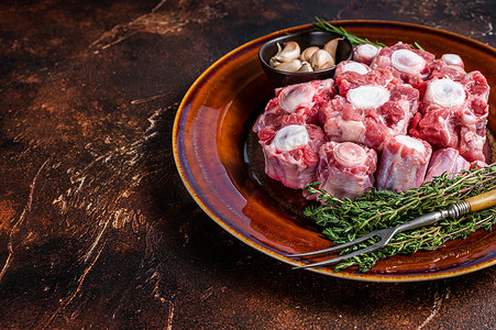 新鲜的未煮过的牛尾牛肉用香草在质朴的盘子上切肉。