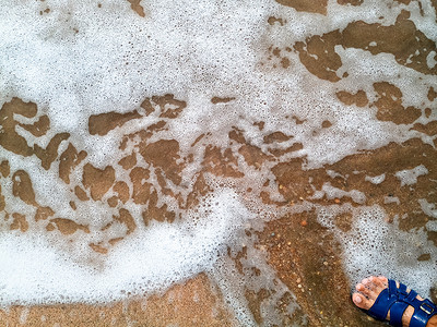 莫尔波在沿海沙子上，海浪的背景纹理和沙子上的泡沫。