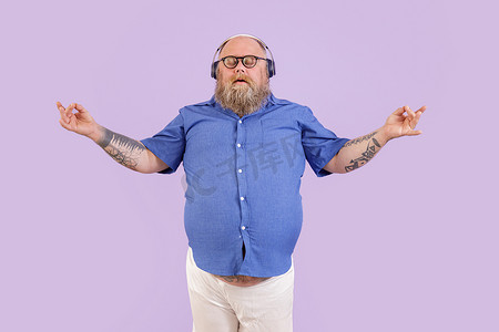 紫色背景音乐摄影照片_安静的肥胖男人在紫色背景下沉思，听轻松的音乐