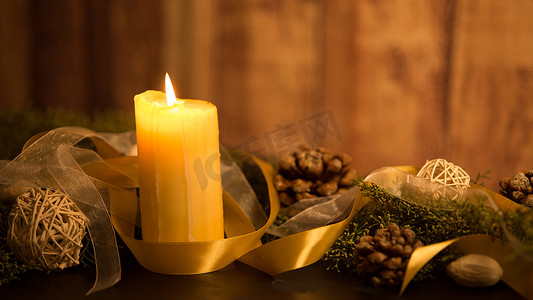 圣诞节概念的温暖：深色木桌上点着三支蜡烛，质朴的木质环境中有松枝、天然松果、金色缎面和白色透明硬纱丝带