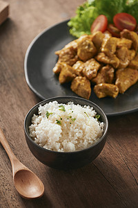 黑白米饭摄影照片_木桌上黑盘中的白米饭、咖喱和鸡肉