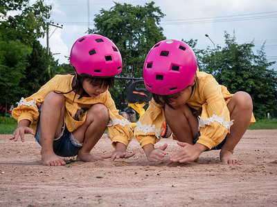 阳光明媚的夏日，两个戴着头盔的可爱小姐妹在公园里玩沙子，骑自行车练习后休息一下。