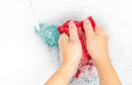 湿衣服摄影照片_女手在水槽里用带复制空间的泡沫洗红衣服