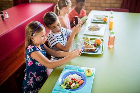 食堂摄影照片_孩子们在午餐时使用科技产品