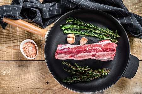 牛仔骨摄影照片_新鲜的生牛肉排骨肉在平底锅上加香草。