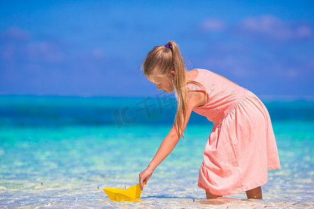 在绿松石海中玩折纸船的小女孩