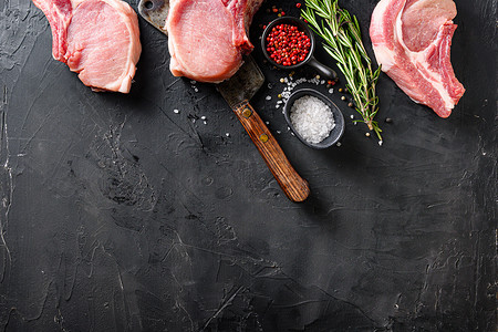 有机猪肉排设置在美国经典屠刀或切肉刀上，在黑色石板桌面视图上配有香料、迷迭香和红辣椒。