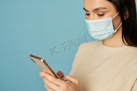 手机病毒摄影照片_戴着面具的年轻女士使用智能手机在工作室里看屏幕