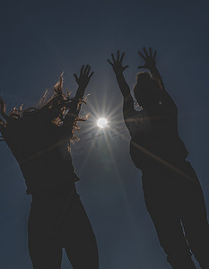 两名年轻女子举起双手向太阳跳跃的剪影。