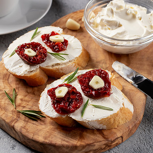 方形图像摄影照片_橄榄木板上自制的三明治，包括奶油奶酪和晒干的西红柿 — 美味的健康早餐、意大利美食、方形图像