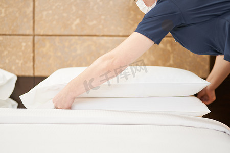 女服务员在酒店房间的床上放干净的枕头