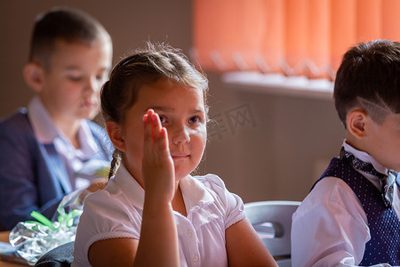 一年级学生坐在她的课桌前，举起手，想回答老师的问题。