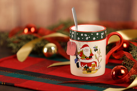 圣诞杯的特写，圣诞桌布上挂着空茶标签，周围有松枝、红色小玩意，木质背景上悬挂着圣诞装饰，具有散景效果