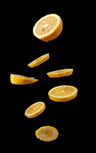 多汁口味摄影照片_成熟多汁的黄色柠檬片漂浮在黑色的空气中