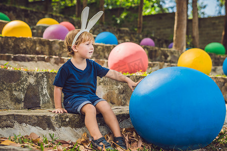太阳户外摄影照片_可爱的小男孩，长着兔耳朵，在户外玩传统的复活节彩蛋。