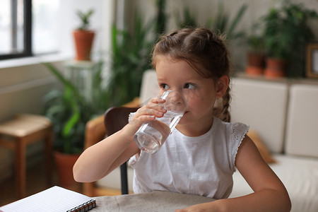 快乐的小女孩在玻璃杯里喝水晶矿泉水，小孩建议每天服用干净的水