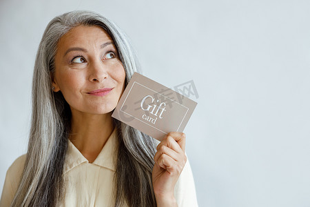 梦幻灰色摄影照片_梦幻般的灰发亚洲女性在工作室里拿着礼品卡靠近脸