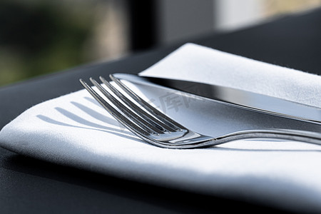 精美菜单摄影照片_户外豪华餐厅餐桌上配有白色餐巾的叉子和刀、婚礼或活动的精美餐饮菜单以及餐饮服务理念
