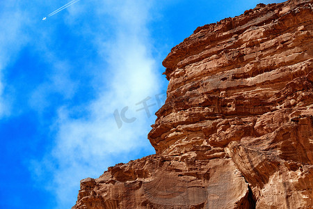 尾迹摄影照片_在瓦迪拉姆自然保护区的沙漠中切割巨石，在天空中用一架产生尾迹的飞机，约旦