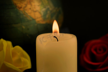 燃烧的黄色蜡蜡烛、地球仪和玫瑰