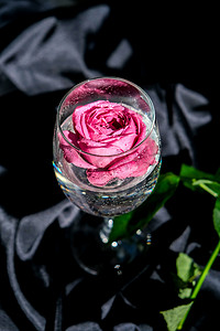 酒杯里装满了粉红色的花瓣，桌子上铺着黑色的丝绸织物。
