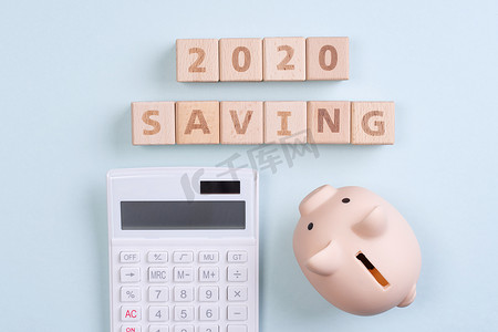 钱几何摄影照片_摘要2020年财务目标设计概念 — 蓝色桌子背景上的几何木块立方体，带存钱罐、顶视图、平躺、复制空间。