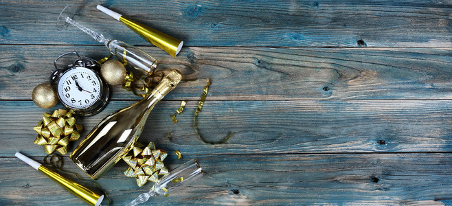 新年快乐的俯视图，金色装饰加上香槟酒瓶和蓝色褪色木头上的眼镜