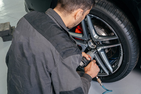 汽车汽车轮胎摄影照片_汽车修理厂的机械更换车轮使用电钻松开螺栓。服务或更换的概念。
