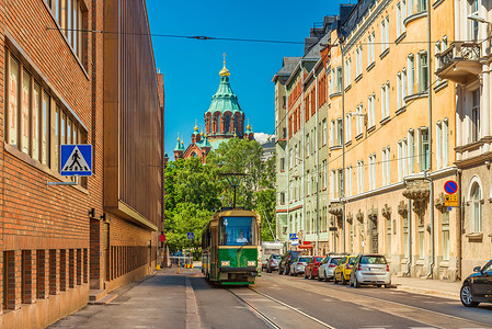 赫尔辛基的一条街道，有一辆老式电车、停放的汽车、色彩缤纷的历史建筑和芬兰乌斯别斯基大教堂